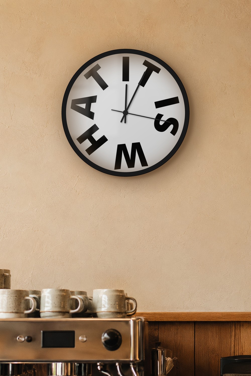 "It is what" wall clock in light neutral and black, on a wall