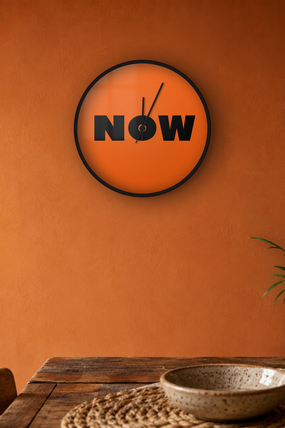 "now" wall clock in orange and black, on a wall