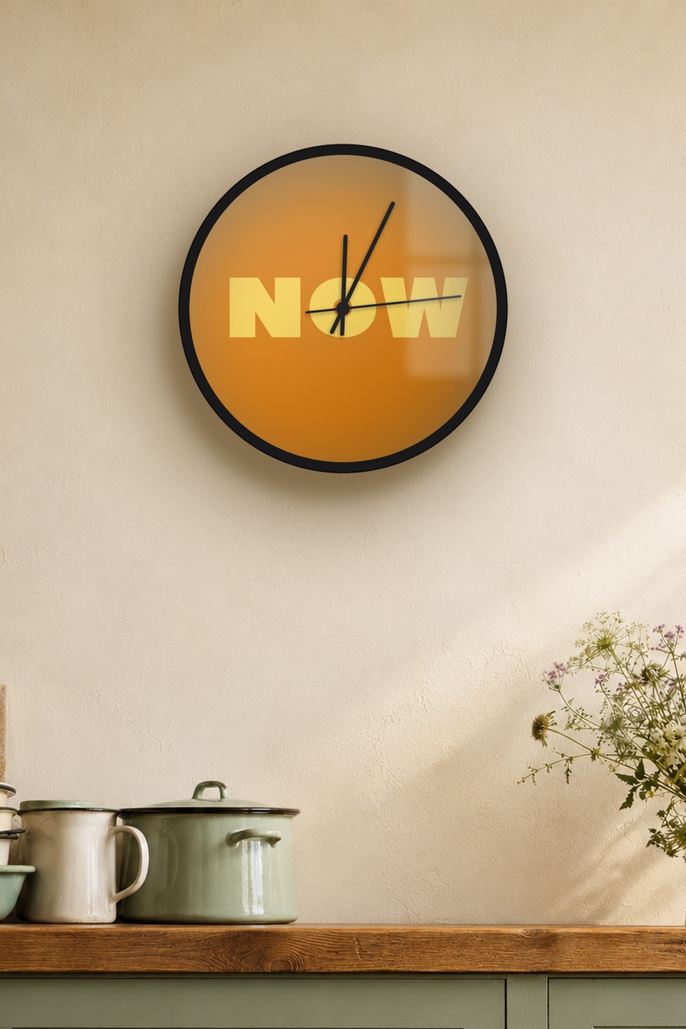 "now" wall clock in amber and light amber, on a wall
