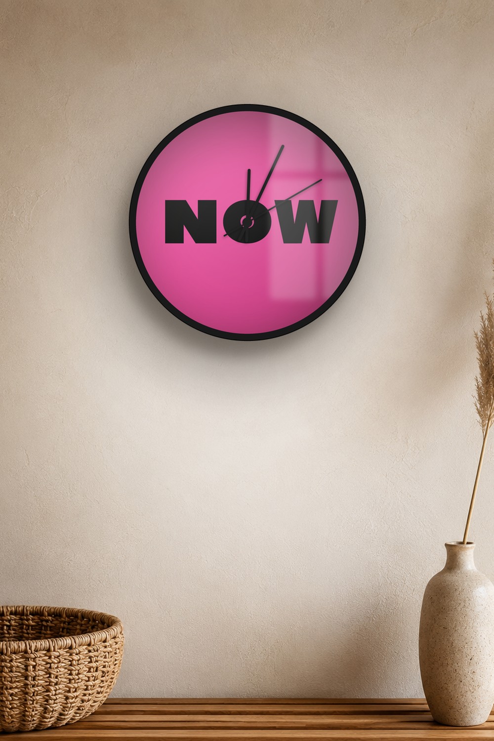 "now" wall clock in pink and black, on a wall