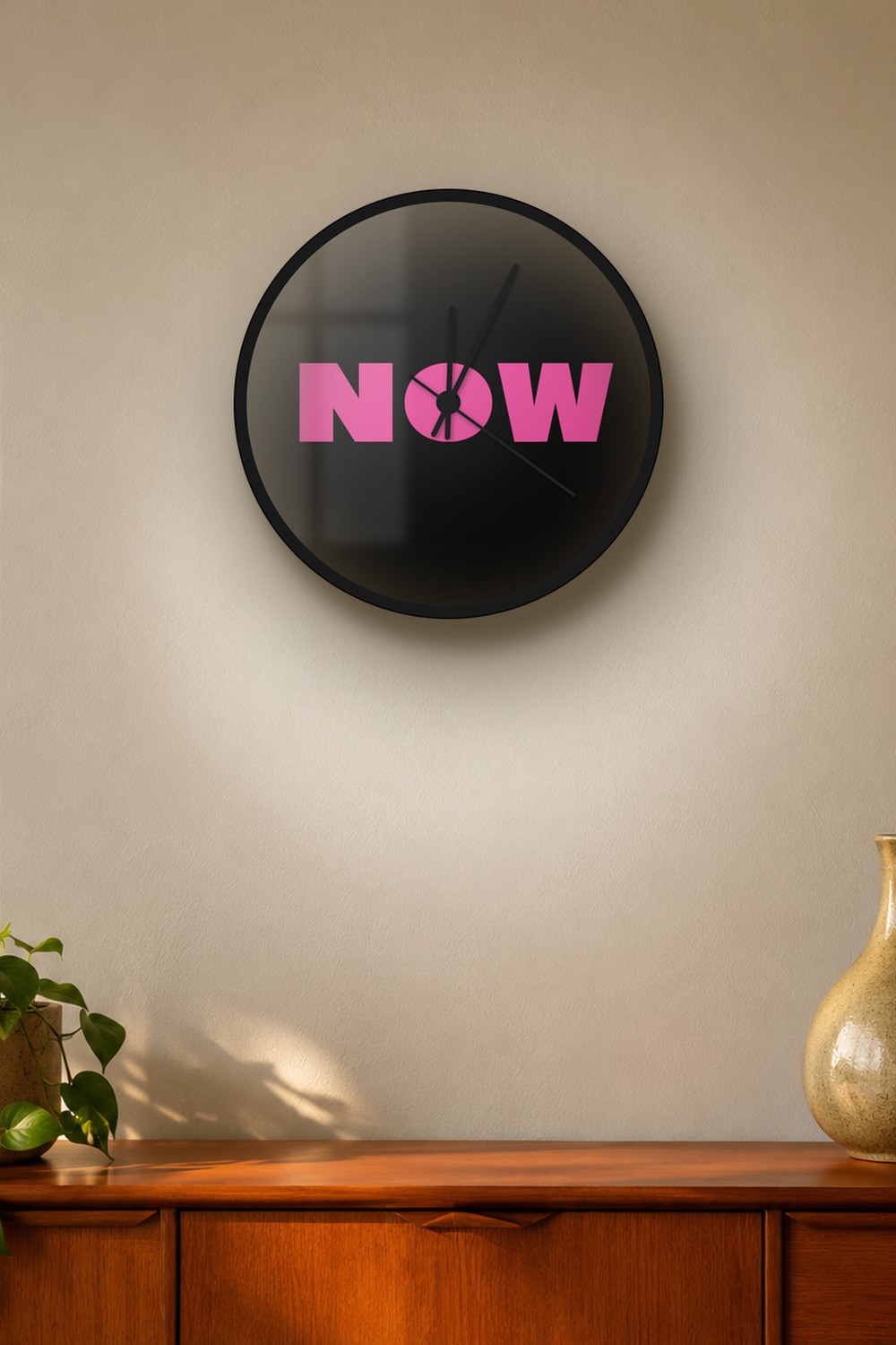 "now" wall clock in black and pink, on a wall