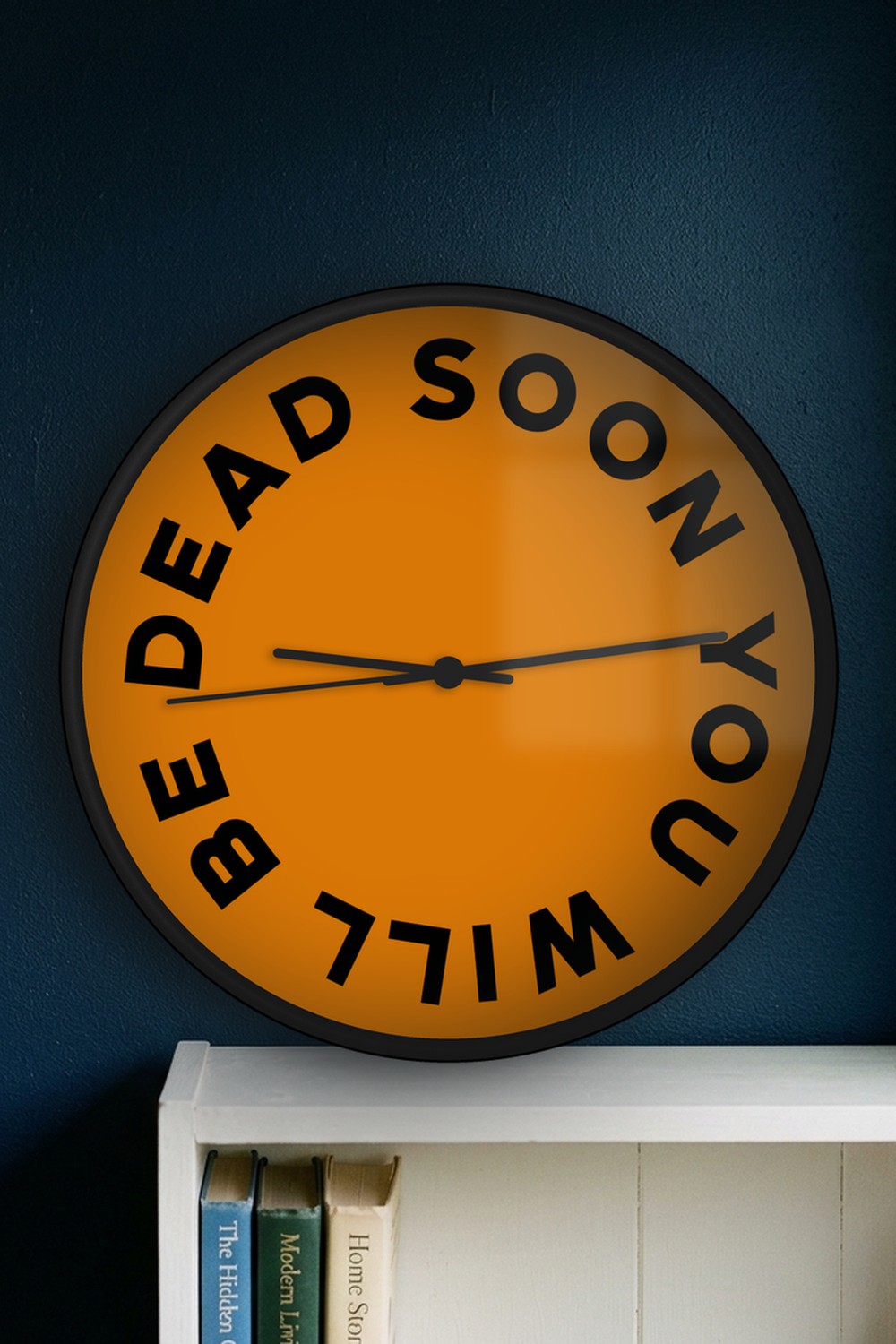 "Soon you will be dead" wall clock in amber and black, on a wall